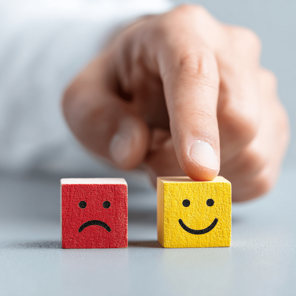 Deux cubes en bois représentant les émotions, avec une main choisissant le cube jaune souriant — symbole de rebond professionnel, d’accompagnement de carrière et de transition réussie après un outplacement ou une reconversion professionnelle.